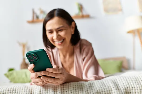 A woman in cozy homewear relaxes on a bed, engrossed in her cell phone. — Stock Photo