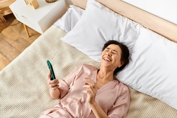A mature woman in cozy homewear lays on a bed, holding a toothbrush. — Stock Photo