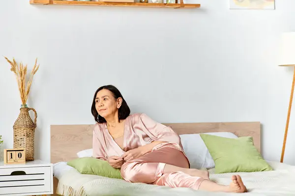 A mature woman in cozy homewear relaxing on top of a bed in a serene room. — Stock Photo