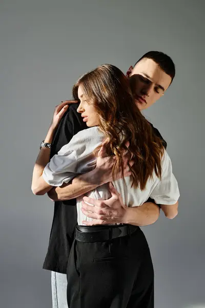 A young man and woman in love embracing each other, captured in an intimate moment against a grey studio backdrop. — Stock Photo