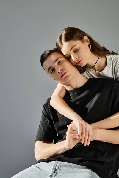 Un hombre muestra su fuerza y amor cargando a una mujer en su espalda contra un fondo gris del estudio. - foto de stock