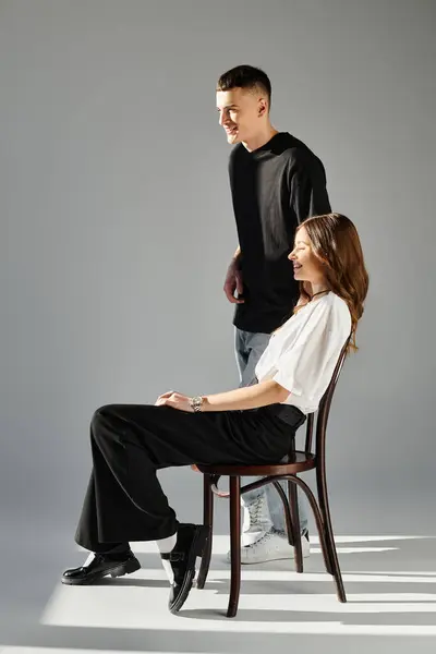 A woman and a man, a young couple in love, sit on chairs in a studio with a grey background. — Stock Photo