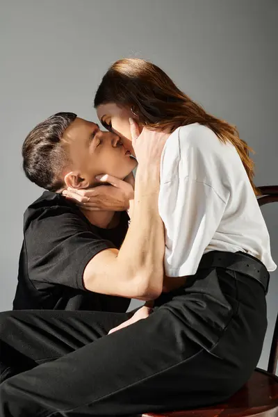 Un hombre y una mujer besándose apasionadamente en un ambiente de estudio, envueltos en amor y conexión contra un fondo gris. — Stock Photo