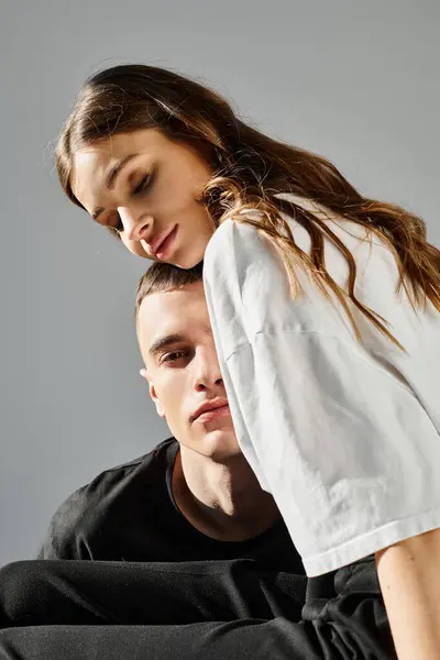 Um homem e uma mulher sentados juntos em cima de uma cadeira num estúdio com um fundo cinzento. — Fotografia de Stock