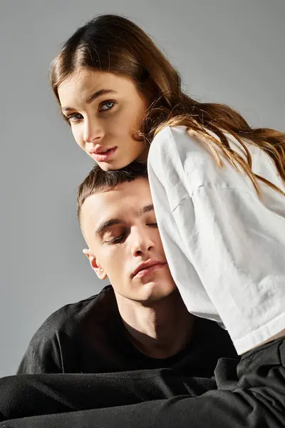 A man sitting beside a woman who is playfully covering her eyes with her hands, both smiling in a studio with a grey background. — Stock Photo
