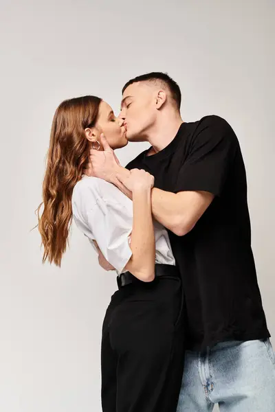 Un giovane uomo e una giovane donna condividono un bacio appassionato in uno studio con uno sfondo grigio. — Foto stock