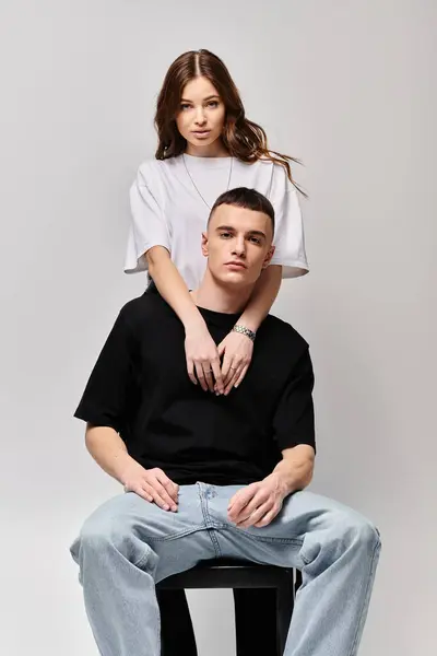 A man perched atop a chair next to a woman, both engaged in deep conversation in a studio with a grey background. — Stock Photo