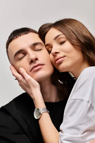 Una joven pareja, hombre y mujer, abrazándose amorosamente en un estudio con un fondo gris. - foto de stock