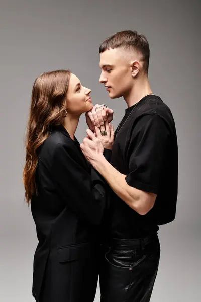 Un giovane uomo e una giovane donna stanno fianco a fianco, trasudando amore e unità in uno studio dallo sfondo grigio. — Foto stock