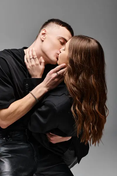 A loving young man and woman sharing a heartfelt kiss in a studio, against a grey background. — Stock Photo