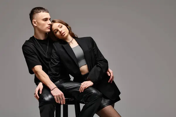 Un hombre y una mujer, una pareja joven, sentados juntos en una silla en un estudio con un fondo gris. - foto de stock