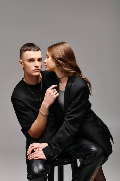 A young man and woman sitting closely together on a stool in a studio with a grey background. — Stock Photo