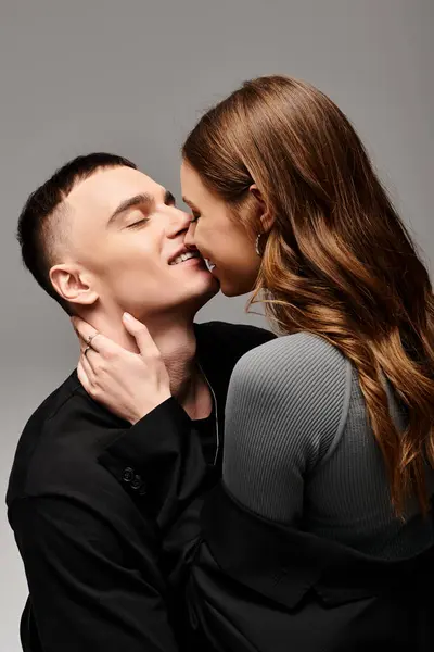 A man gently kisses a woman on the cheek, showing affection in a studio setting with a grey background. — Stock Photo
