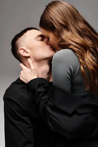 A man and woman share a romantic kiss in a studio, expressing their love for each other against a grey background. — Stock Photo