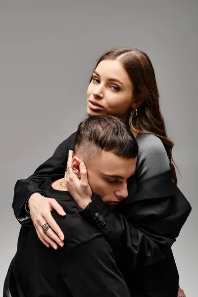 Una giovane coppia avvolta in un caldo abbraccio, che esprime amore e vicinanza in uno studio dallo sfondo grigio. — Foto stock