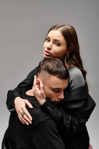 A young couple wrapped in a warm hug, expressing love and closeness in a studio with a grey background. — Stock Photo