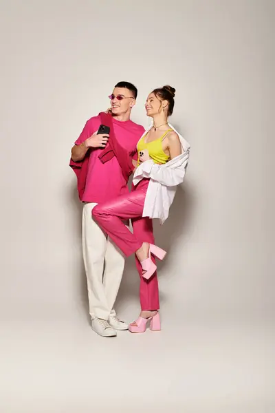 A stylish young couple in love, dressed in pink and white, poses together in a studio against a grey background. — Stock Photo