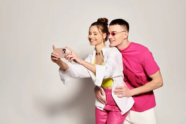 Jeune couple élégant sourit tout en prenant un selfie avec un téléphone portable dans un studio sur un fond gris. — Photo de stock