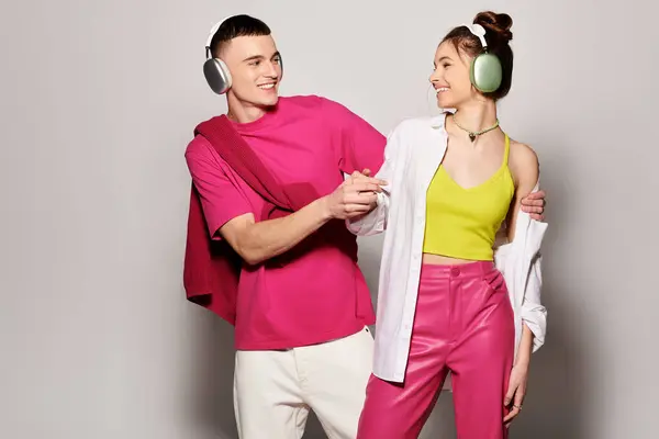 A fashionable man and woman, wearing headphones, stand next to each other in a studio with a grey background. — Stock Photo