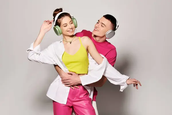A stylish young couple in love wearing headphones, immersed in the music, against a grey studio background. — Stock Photo