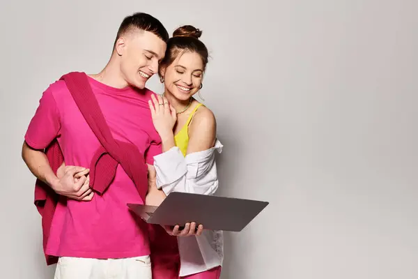 Una giovane coppia di eleganti stand con computer portatile fianco a fianco in uno studio con uno sfondo grigio. — Foto stock
