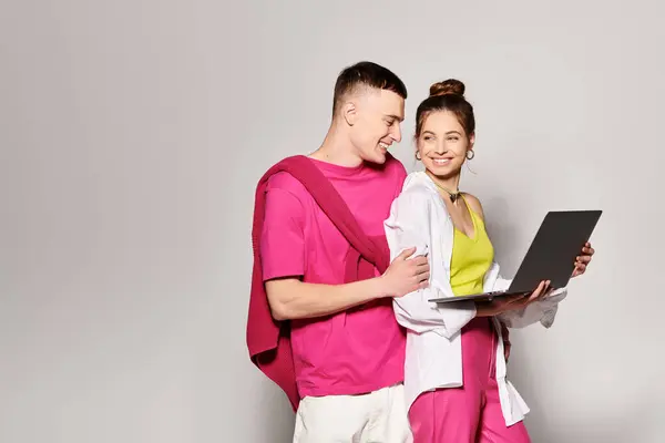A stylish young couple in love, engaged with a laptop, exploring and discovering together in a studio with a grey background. — Stock Photo