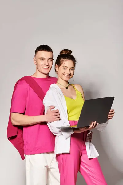 Un uomo e una donna che lavorano insieme su un computer portatile in uno studio con uno sfondo grigio, mettendo in mostra il lavoro di squadra e la partnership. — Foto stock