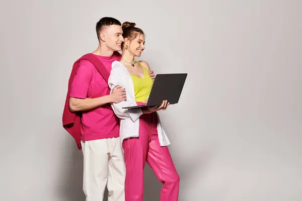 Stilvolle junge Männer und Frauen, die zusammen mit einem Laptop auf dem Bildschirm in einem Studio mit grauem Hintergrund stehen. — Stockfoto