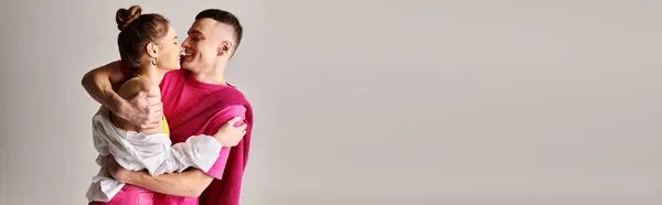 A stylish young man tenderly holds his partner in his arms against a grey studio backdrop. — Stock Photo