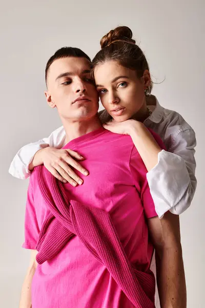 Um jovem casal elegante apaixonado, o homem gentilmente mantém a mulher vestida de rosa contra um fundo de estúdio cinza. — Fotografia de Stock