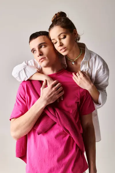 Stylish young couple in love, man demonstrates strength by carrying woman on his back in studio with grey background. — Stock Photo