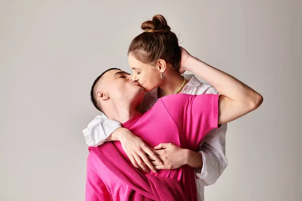 A woman in a pink dress embraces a man in a white shirt, expressing love and closeness in a stylish studio setting with a grey background. — Stock Photo