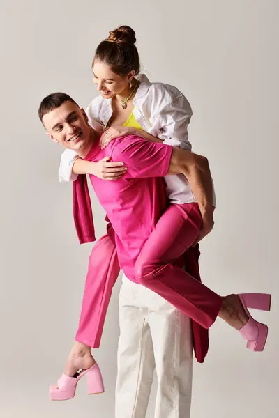 Un jeune homme élégant tient tendrement une femme dans ses bras sur un fond de studio gris. — Photo de stock