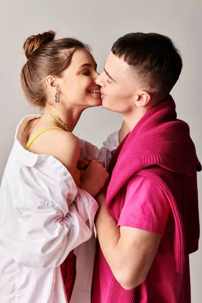 Un giovane uomo e una donna alla moda condividono un bacio appassionato in uno studio su uno sfondo grigio. — Foto stock