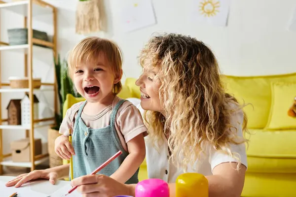 Une mère aux cheveux bouclés et sa fille tout-petit participent à des activités Montessori à une table dans un cadre confortable à la maison. — Photo de stock