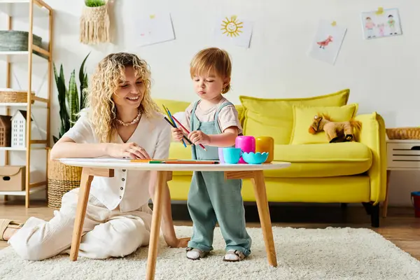 A curly mother and her toddler daughter sit at a table, engaging in Montessori learning activities together at home. — Stock Photo