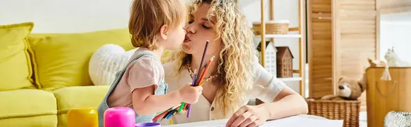 Une mère aux cheveux bouclés embrasse amoureusement sa petite fille sur la joue dans une maison confortable en utilisant la méthode d'éducation Montessori. — Photo de stock