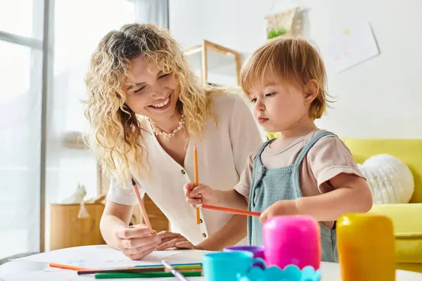 Une mère aux cheveux bouclés et sa fille en bas âge explorent la créativité en utilisant des crayons de couleur dans un cadre confortable à la maison. — Photo de stock