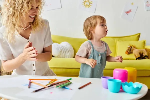 Кучерявая мать и ее малышка дочь с радостью участвуют в красочной творческой деятельности с карандашами с помощью метода Монтессори дома. — стоковое фото