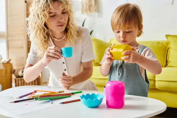 Une mère aux cheveux bouclés et sa petite fille sont assises à une table, absorbées par les activités d'apprentissage de Montessori à la maison. — Photo de stock