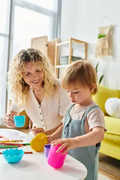 A curly mother and her toddler daughter engage in playful Montessori cup activities at home. — Stock Photo