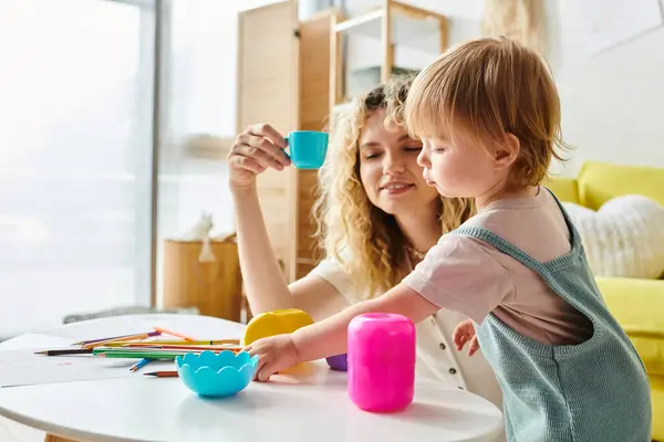 Uma mãe encaracolada e sua filha criança se envolver em exploração lúdica com copos coloridos em casa, abraçando o método Montessori. — Fotografia de Stock
