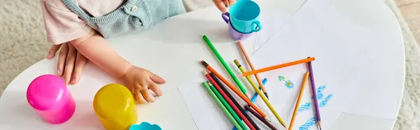 Toddler girl happily sits at a table, engrossed in play with colored pencils. — Stock Photo