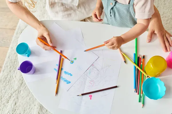 Toddler and mom sit at a table drawing with colorful pencils and crayons. — Stock Photo