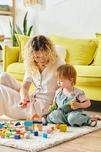 Une mère bouclée joue joyeusement avec sa petite fille sur le sol à la maison, en utilisant la méthode d'éducation Montessori. — Photo de stock