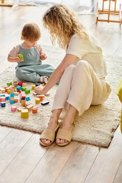 Кучерявая мать сидит на полу, общаясь с малышом дочь с помощью метода Монтессори образования на дому. — стоковое фото
