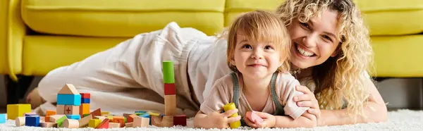 A woman with curly hair lays on the floor with her toddler daughter, engaging in the Montessori method of education at home. — Stock Photo