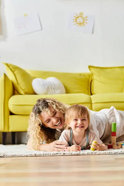 A curly mother and her toddler daughter embrace while practicing the Montessori method of education at home. — Stock Photo