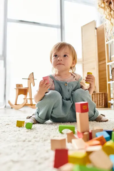 Little girl sits on the floor, engrossed in building with colorful blocks, embodying the Montessori method. — Stock Photo