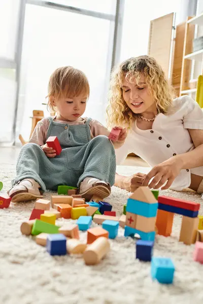 Кучерявая мать и ее малышка дочь сближаются и учатся играть с блоками на полу дома. — стоковое фото